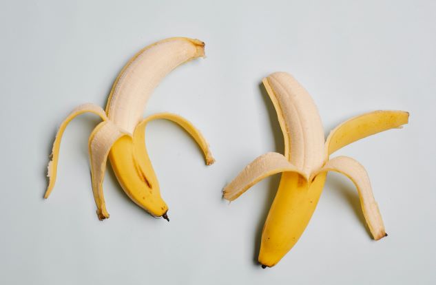 Dva banány leží vedle sebe na bílé podložce.